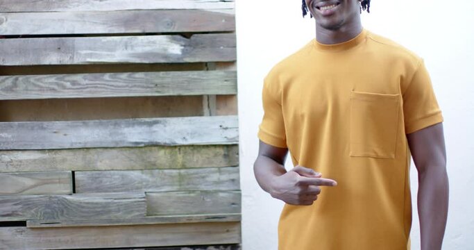 Happy african american man wearing yellow t shirt pointing to pocket, slow motion, copy space