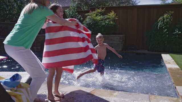 Mother covers kids up with beach towels as they get out of the pool