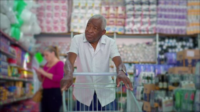 One senior black shopper pushing shopping cart at grocery store, browsing products on shelves depicting consumer lifestyle habits