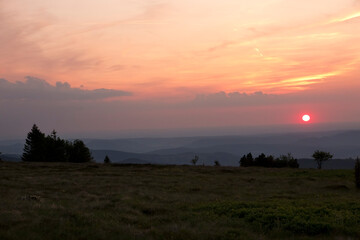 Sunset over de hills of the Vosges, an orange colored sun in the evening sky, hill ranges fading in...