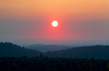 Sunset over de hills of the Vosges, an orange colored sun in the evening sky, hill ranges fading in...