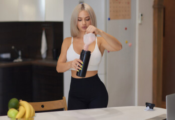 Young woman preparing protein shake at table in kitchen.
