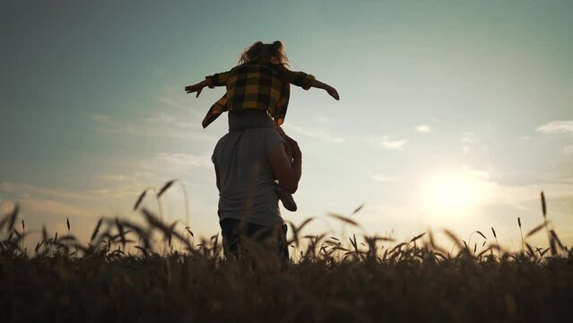 Happy family father and daughter cheerful walk at sunset in nature. Girl child joyfully sit on dad neck. Kid and parent in field in countryside walk in summer. Active lifestyle with smile on your face