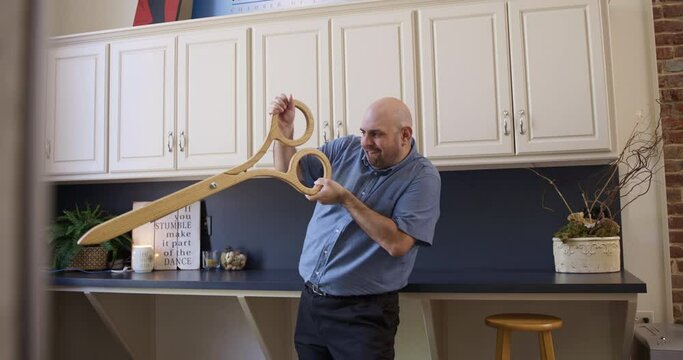 Bald man plays with comically large scissors in an office kitchen