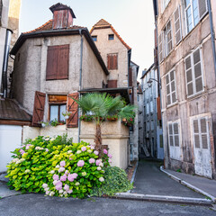 Fototapeta na wymiar Picturesque alley with old stone houses and colorful flowers at the entrance of the houses, Pau, France.