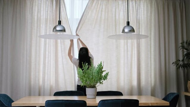 Back view, woman closes light curtains in the living room