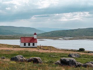 Small traditional, white, wooden church with red roof in the field. Church in Iceland.