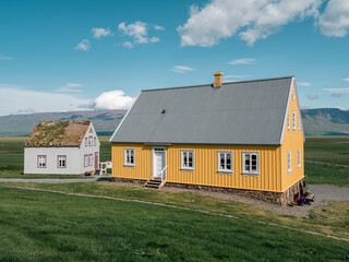 Traditional turf covered house in Glaumbaer, northwestern Iceland. Agricultural fields with horses, and snow-covered mountains in the background