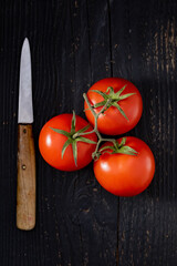 Fresh tomatoes over a black wodden table near a knife