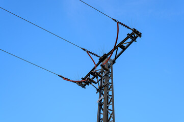 A three phase power line pylon terminates into a ground cable with anti bird spikes on top and red...