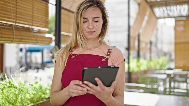 Young blonde woman waitress smiling confident using touchpad at coffee shop terrace