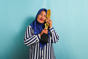 An excited middle-aged Asian businesswoman in a blue hijab and a striped shirt is hugging a gold...