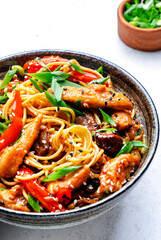 Stir fry noodles with chicken slices, red paprika, mushrooms, chives, soy sauce and sesame seeds in ceramic bowl. Asian cuisine dish. White table background, top view