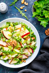 Waldorf salad with fresh apple, celery, lettuce, grilled chicken fillet, arugula and walnuts on plate, blue table background, top view