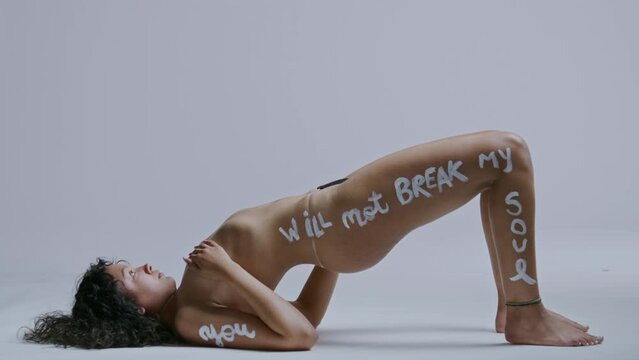 Hispanic woman with body pain lifts her bare body off the ground on a white backdrop