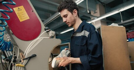 A red-haired man in a blue uniform is polishing the soles of shoes, removing manufacturing flaws. The final stage of shoe production, shoe repair in a textile factory