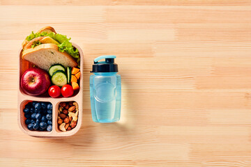 Kids school lunch box with sandwich, fruits, vegetables, blueberries, nuts and bottle of water on wooden table