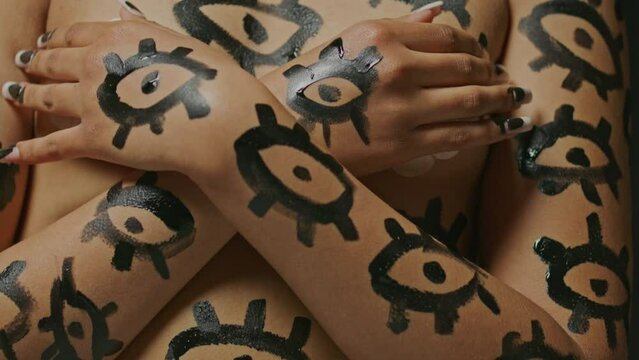Woman without clothes looks at the camera with painted eye designs painted on her body