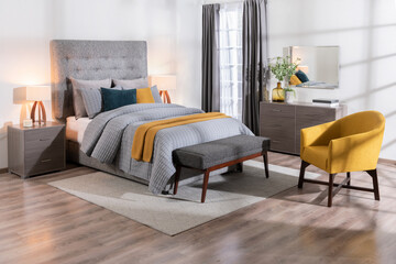 A modern bedroom featuring a large bed, a yellow chair, a dresser, and a wooden bench, a cozy...