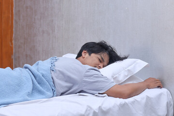 Tired man sleeping in prone position on white bed at home. Need rest. 