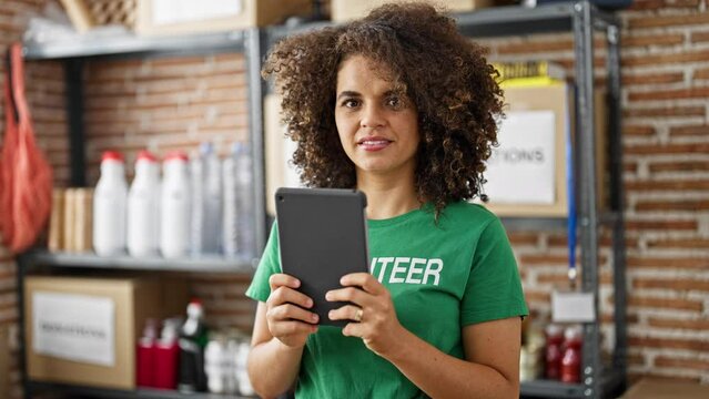 Young beautiful hispanic woman volunteer smiling confident using touchpad at charity center