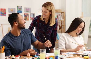 Fototapeta premium Artist teaching her students to paint at table in studio. Creative hobby