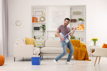 Spring cleaning. Man in headphones with mop singing while tidying up living room