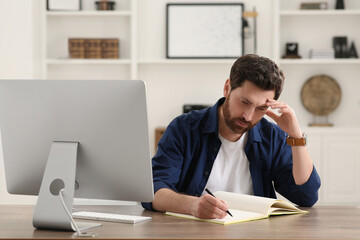 Home workplace. Man taking notes near computer at wooden desk in room