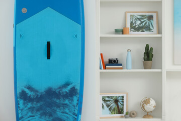 SUP board and shelving unit with different decor elements in room. Interior design
