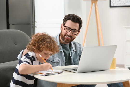 Man working remotely at home. Father using laptop while his son drawing at desk