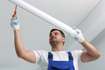 Ceiling light. Electrician installing led linear lamp indoors, low angle view