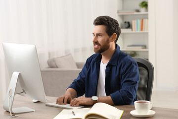 Fototapeta premium Home workplace. Happy man working with computer at wooden desk in room