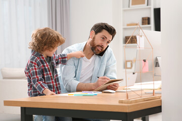 Little boy bothering his father at home. Man working remotely at desk