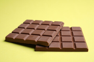 Pieces of tasty milk chocolate bar on pale yellow background