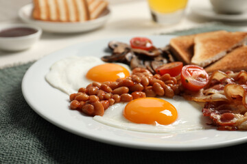 Plate with fried eggs, mushrooms, beans, tomatoes, bacon and toasts on table, closeup. Traditional English breakfast
