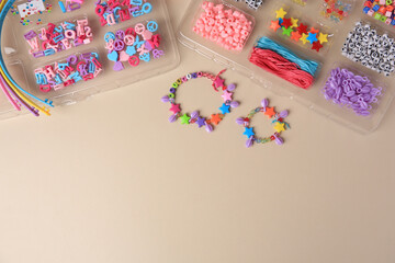 Handmade jewelry kit for kids. Colorful beads, wristbands and bracelets on beige background, flat lay. Space for text