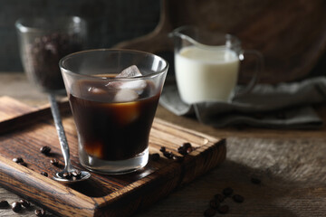 Glass of delicious iced coffee and beans on wooden table, space for text
