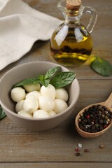 Tasty mozarella balls, basil leaves and spices on wooden table