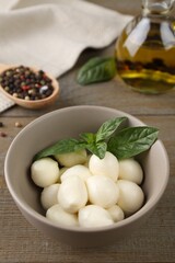 Tasty mozarella balls and basil leaves in bowl on wooden table