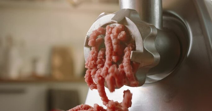 Meat coming through grinder plate. Closeup of minced meat flowing out of meat grinder. Slow motion blurred background kitchen. Advertising. Electric meat grinder in the kitchen burger food chef cook