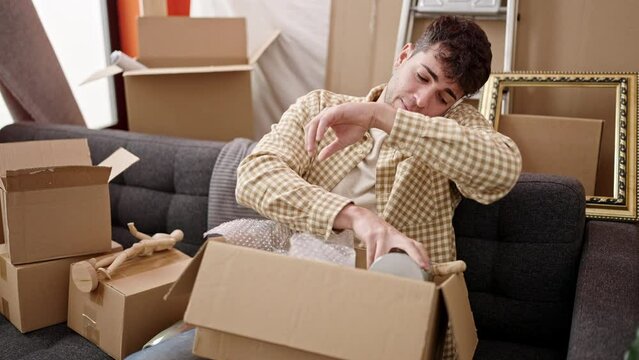 Young hispanic man unpacking cardboard box speaking on the phone at new home