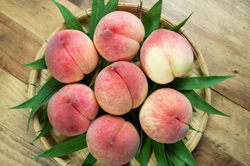 White Peaches with leaves on the wooden table, Fresh Peach in wooden basket on wooden Background.
