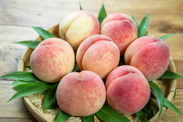 Peaches with leaves on the wooden table, Fresh Peach in wooden basket on wooden Background.