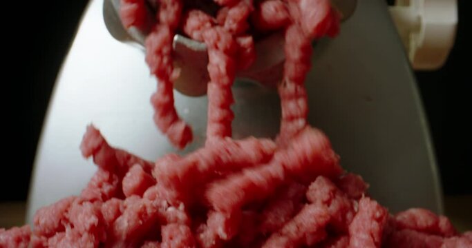 Strings of fresh ground meat falling down grinder is working. Close-up of grinding juicy raw red beef veal. Slow motion black background Advertising. Preparation of minced meat for burger by cook