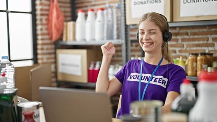 Young blonde woman volunteer having video call sitting on table celebrating at charity center