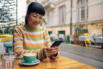 Dark haired japanese girl enjoying her coffee while looking at her mobile phone.