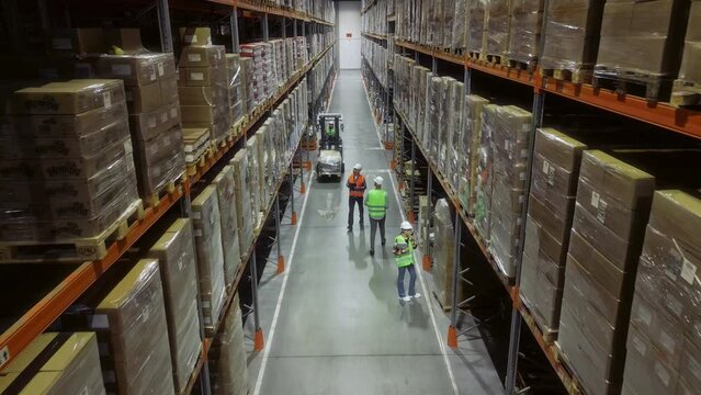 Top-Down Elevating View: Bustling Retail Warehouse, Workers in Safety Gear Working, Stack, and Transport Cardboard Boxes, Ensuring the Smooth Flow of Goods for Distribution