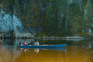 Two fishermen, father and son, are fishing in a motor boat in the summer on a mountain river in good sunny weather. Rest on the river in the men's company. River rafting. High quality photo