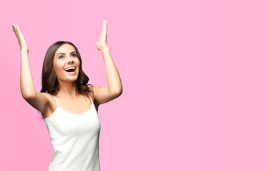 Fototapeta premium Portrait studio image of happy gesturing or praying young beautiful woman looking up, in white casual clothing, isolated over rose pink color background. Copy space area for some text or slogan.
