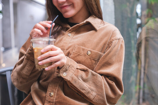 Closeup image of a young woman holding and drinking iced coffee in cafe